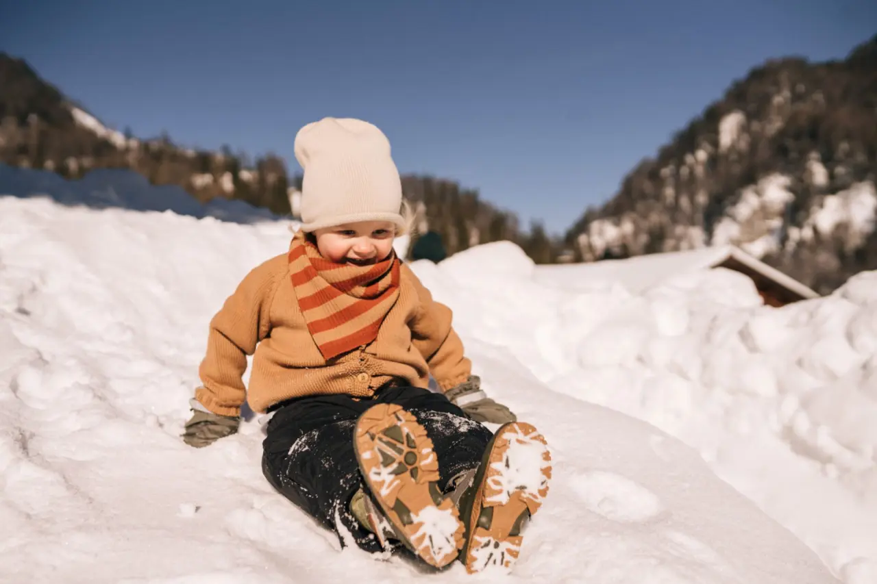 Glückliches Kind spielt im Schnee vor Bergkulisse im POST Family Resort.