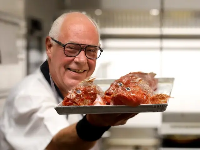 Lachender Koch mit frischem Fisch in der Küche des Hotel Am Hirschhorn, bereit für die Zubereitung von Spezialitäten.