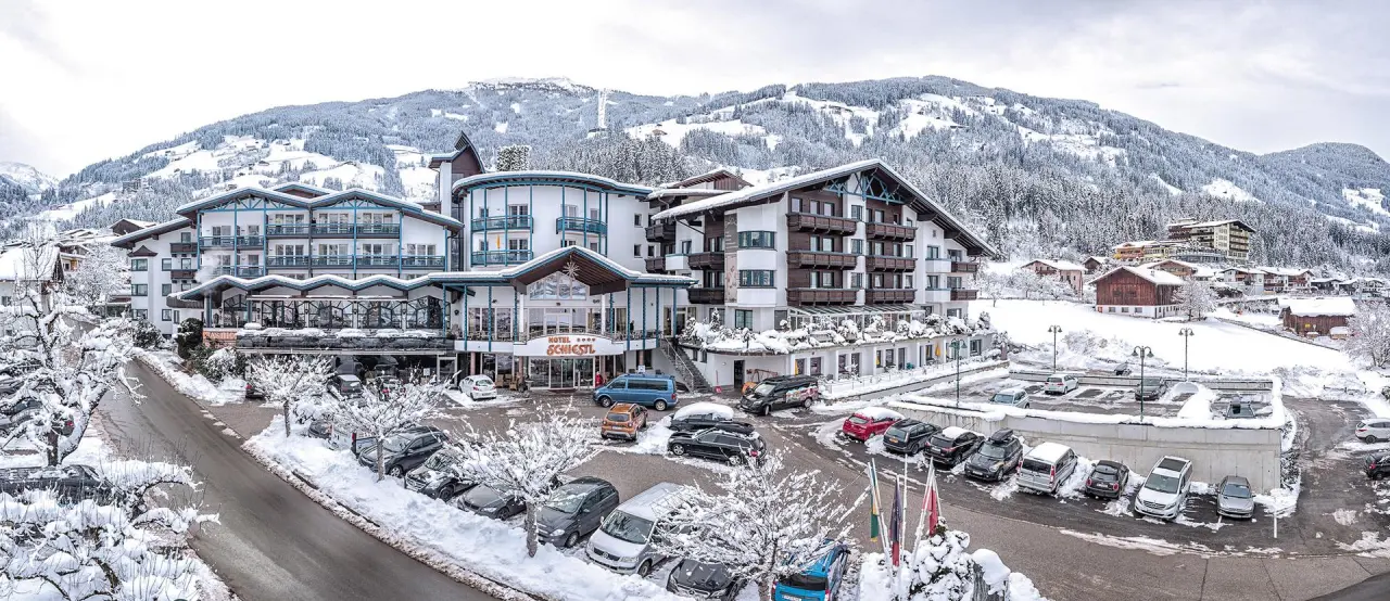 Winterliche Aussenansicht des Wohlfühlhotel Schiestl im Zillertal mit verschneiten Bergen und Parkplatz.
