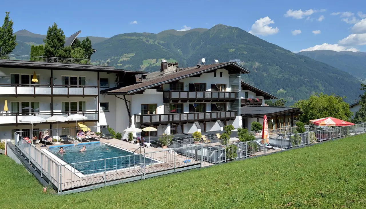 Aussenpool mit Gästen und Sonnenliegen vor dem Wohlfühlhotel Schiestl mit Alpenpanorama.