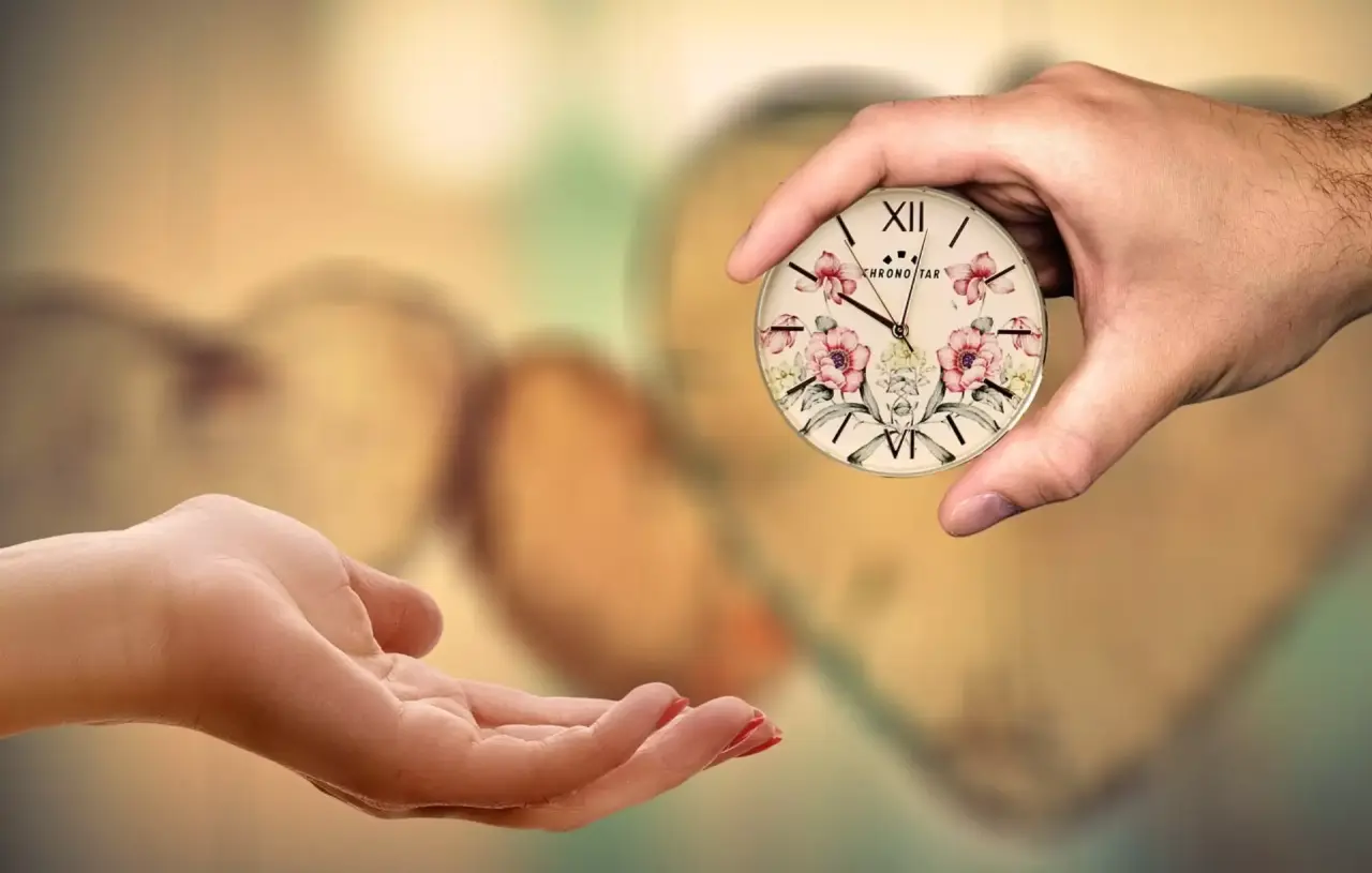 Hände reichen eine dekorative Uhr mit Blumenmuster, als Symbol für wertvolle Zeit im Hotel Schweizer Hof.