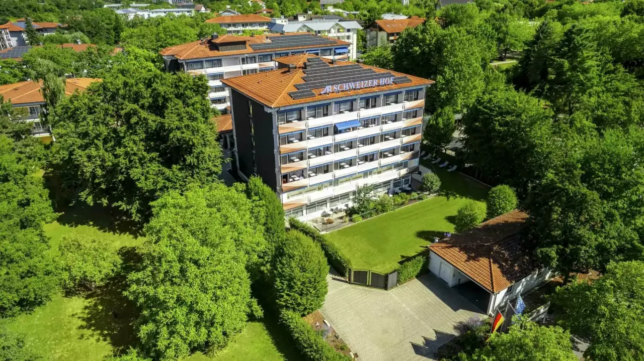 Luftaufnahme des Hotel Schweizer Hof Betriebs-GmbH, umgeben von gruenen Baeumen und mit Solaranlagen auf dem Dach.
