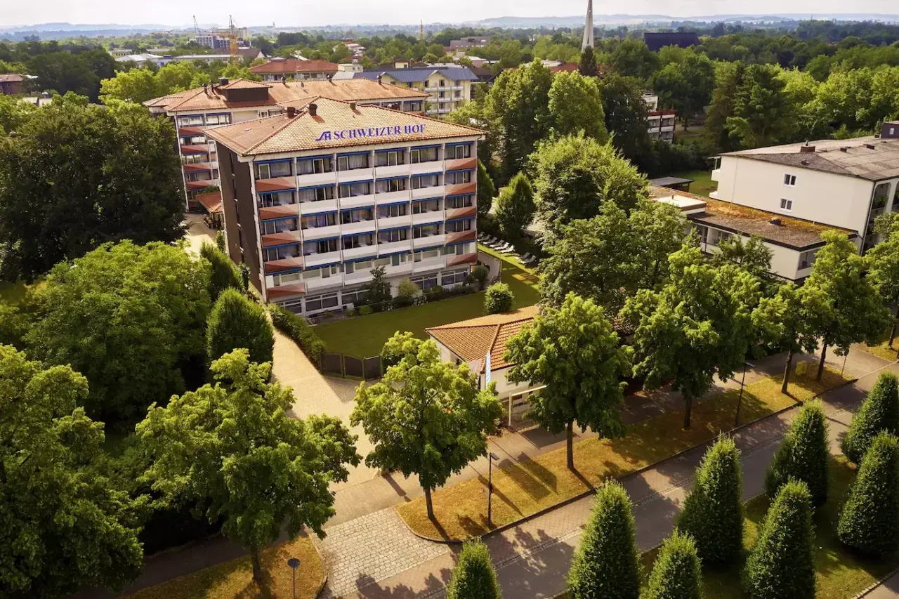 Luftaufnahme des Hotel Schweizer Hof Betriebs-GmbH mit rotem Dach und gruener Umgebung, ideal fuer einen Wellnessurlaub.