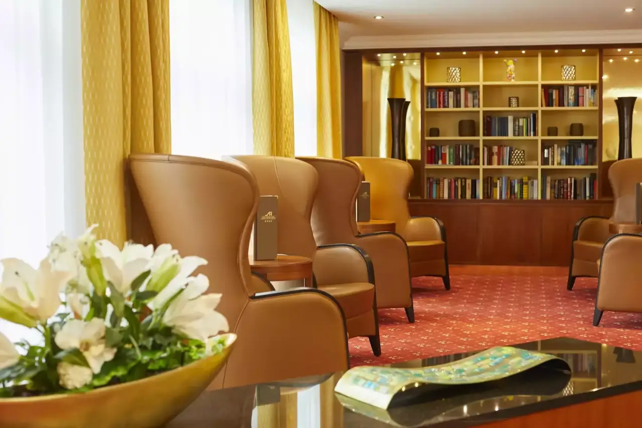Gemütliche Hotellobby des Hotel Schweizer Hof Betriebs-GmbH mit beigen Ledersesseln, Bücherregal und Blumenarrangements.