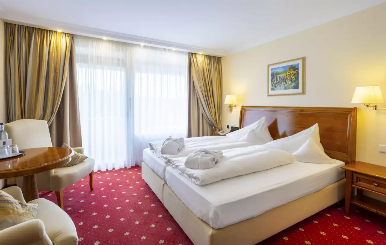 Gemütliches Doppelzimmer im Hotel Schweizer Hof Betriebs-GmbH mit bequemen Betten, Sitzbereich und Balkonzugang.