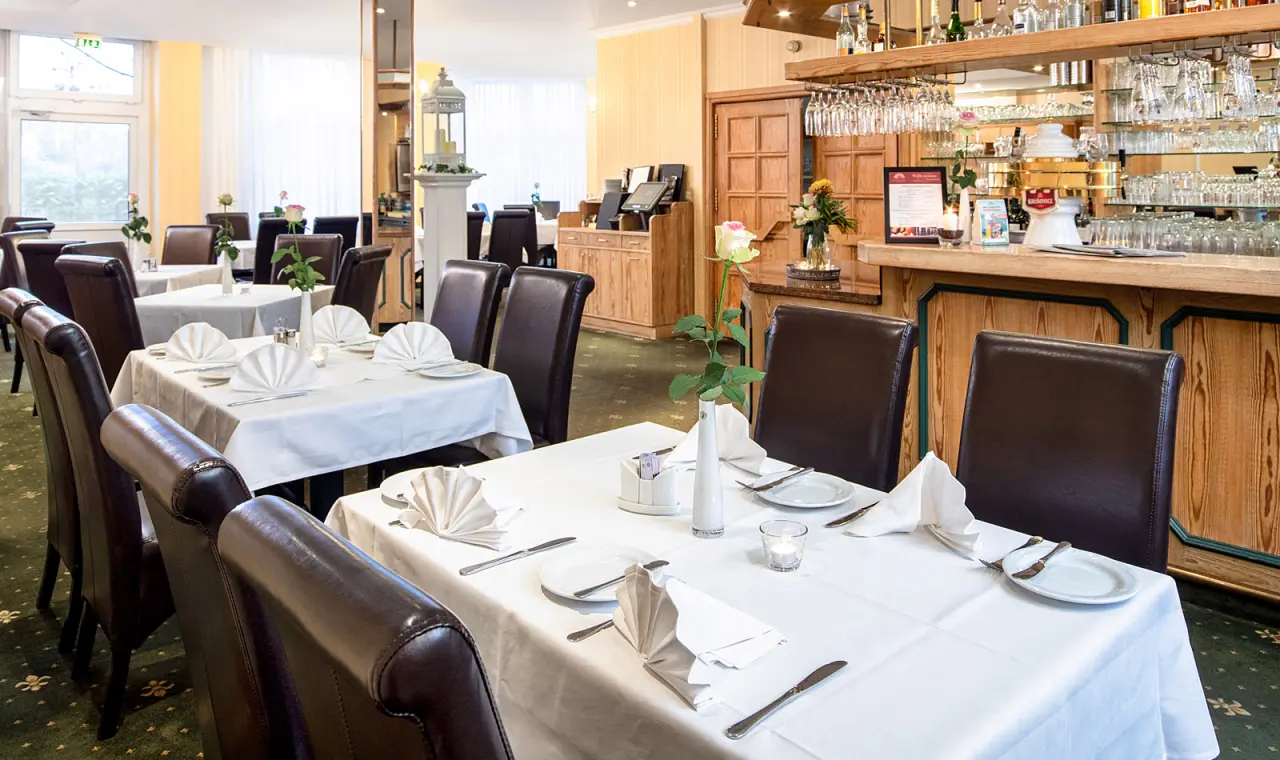 Helles und einladendes Restaurant im Hotel Flora mit elegant gedeckten Tischen und einer Bar, bereit für kulinarische Genüsse.