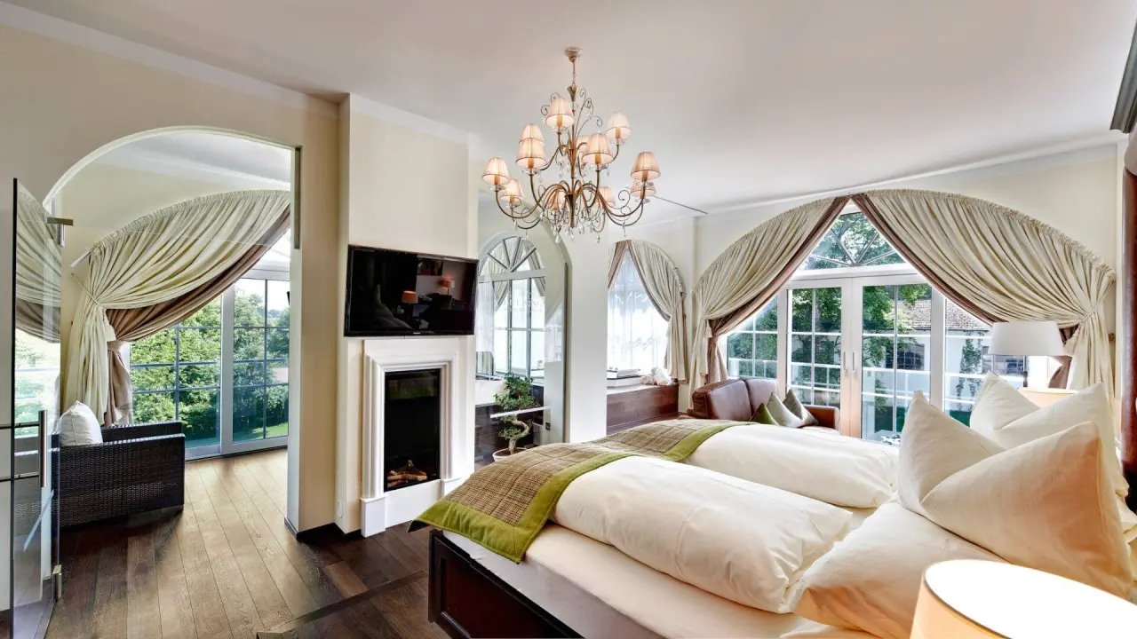 Luxuriöses Doppelzimmer im Gut Ising mit Kamin, TV und großen Fenstern mit Blick ins Grüne. Komfortable Unterkunft.