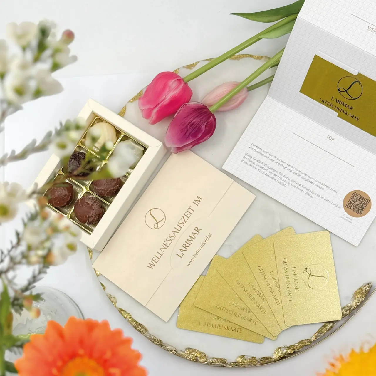 Wellness Gutscheinkarten und Pralinen vom Hotel Larimar mit rosa Tulpen auf einem Tablett, ideal als Geschenk.