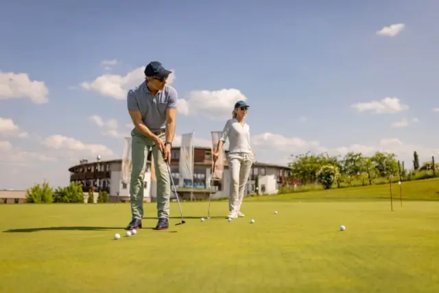Gäste beim Golfen auf dem Putting Green mit dem Hotel Larimar im Hintergrund an einem sonnigen Tag.