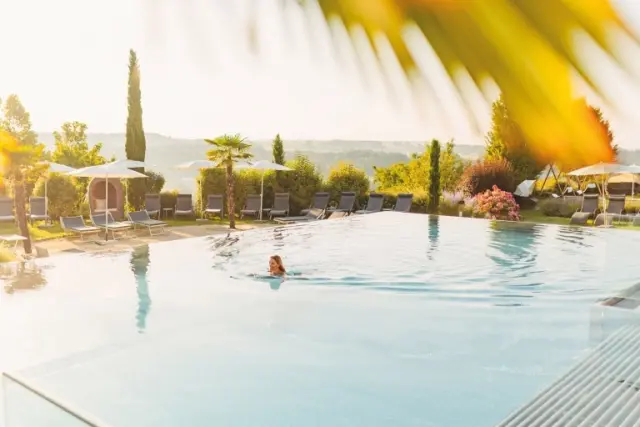 Infinity Pool des Hotel Larimar bei Sonnenuntergang, umgeben von Palmen und Liegen, mit entspannter Badegästin.