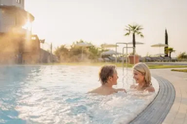 Entspannendes Paar im warmen Aussenpool des Hotel Larimar bei Sonnenuntergang mit Palmen im Hintergrund.