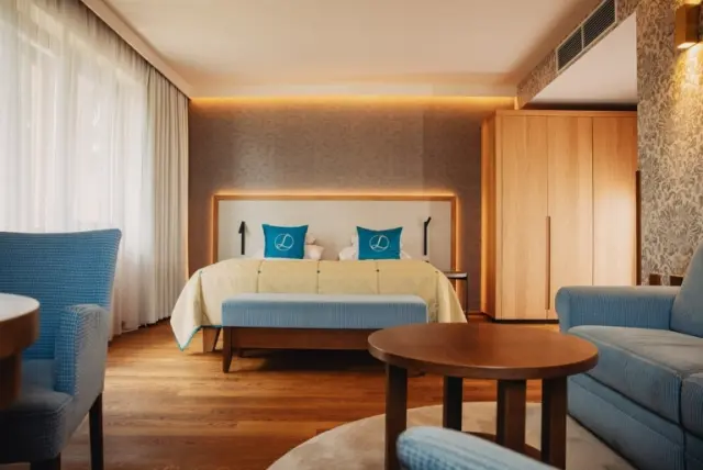 Geräumiges und helles Hotelzimmer im Hotel Larimar mit Doppelbett, Sitzbereich und modernen Holzmöbeln.
