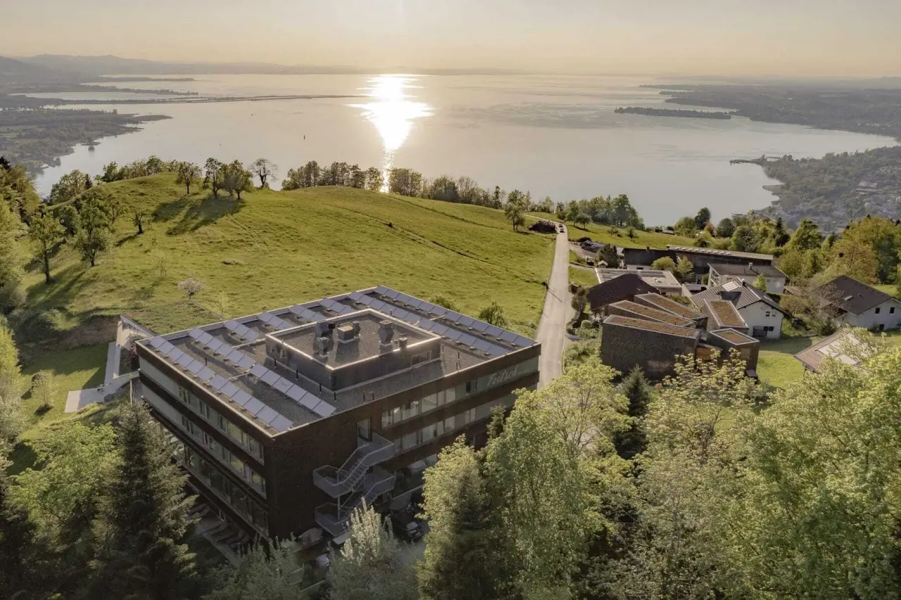 Luftaufnahme des MentalSpa-Resort Fritsch am Berg bei Sonnenuntergang mit Blick auf den Bodensee und grüne Hügel.