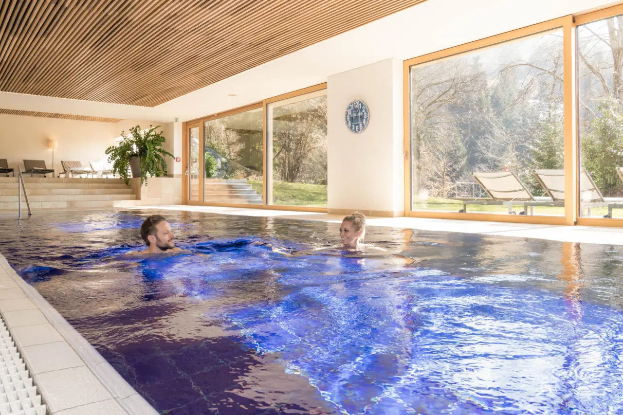 Gäste entspannen im hellen Innenpool des MentalSpa-Resort Fritsch am Berg mit Blick auf die Natur.