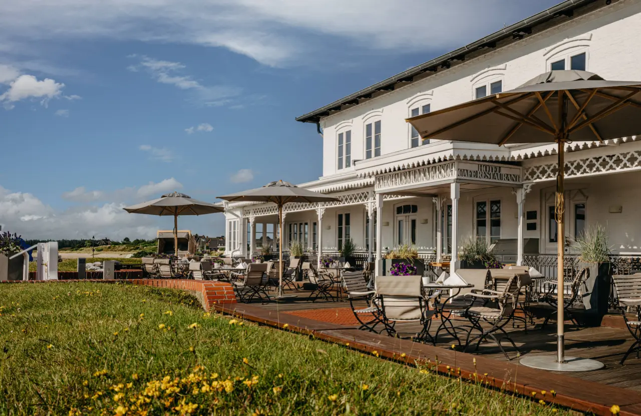 Elegantes Fährhaus Sylt Hotel mit sonniger Restaurantterrasse und Blick auf die Dünenlandschaft.