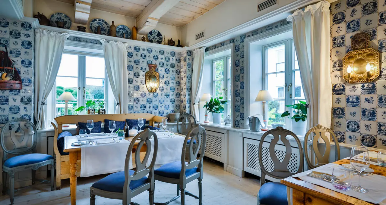 Gemütlicher Restaurantbereich im Fährhaus Sylt mit blau-weißen Fliesen, Holzbalkendecke und gedeckten Tischen.