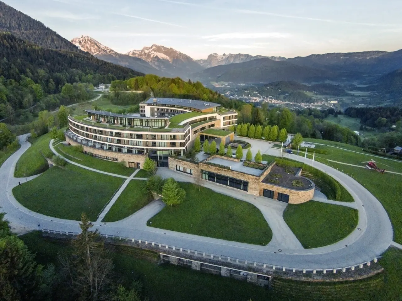 Modernes Luxushotel Kempinski Berchtesgaden in alpiner Landschaft mit grünen Dächern und Bergblick.