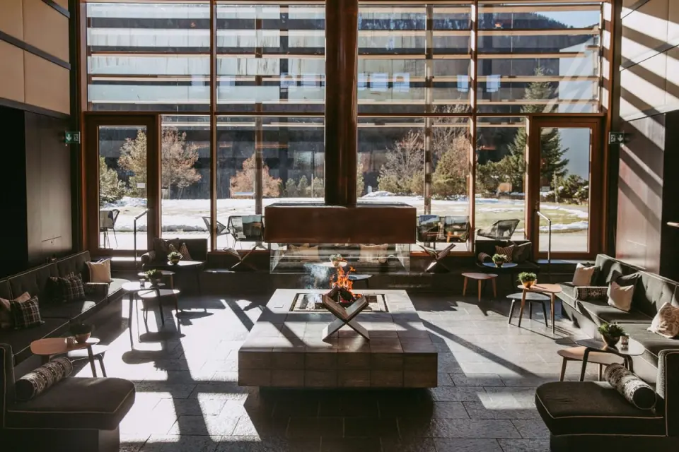 Gemütliche Lobby mit Kamin und Blick auf die verschneite Landschaft im Kempinski Hotel Berchtesgaden.