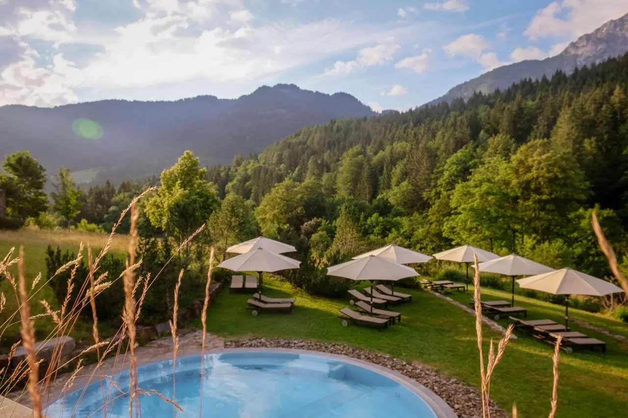 Aussenpool mit Liegewiese und Sonnenschirmen vor beeindruckendem Bergpanorama im Kempinski Hotel Berchtesgaden.