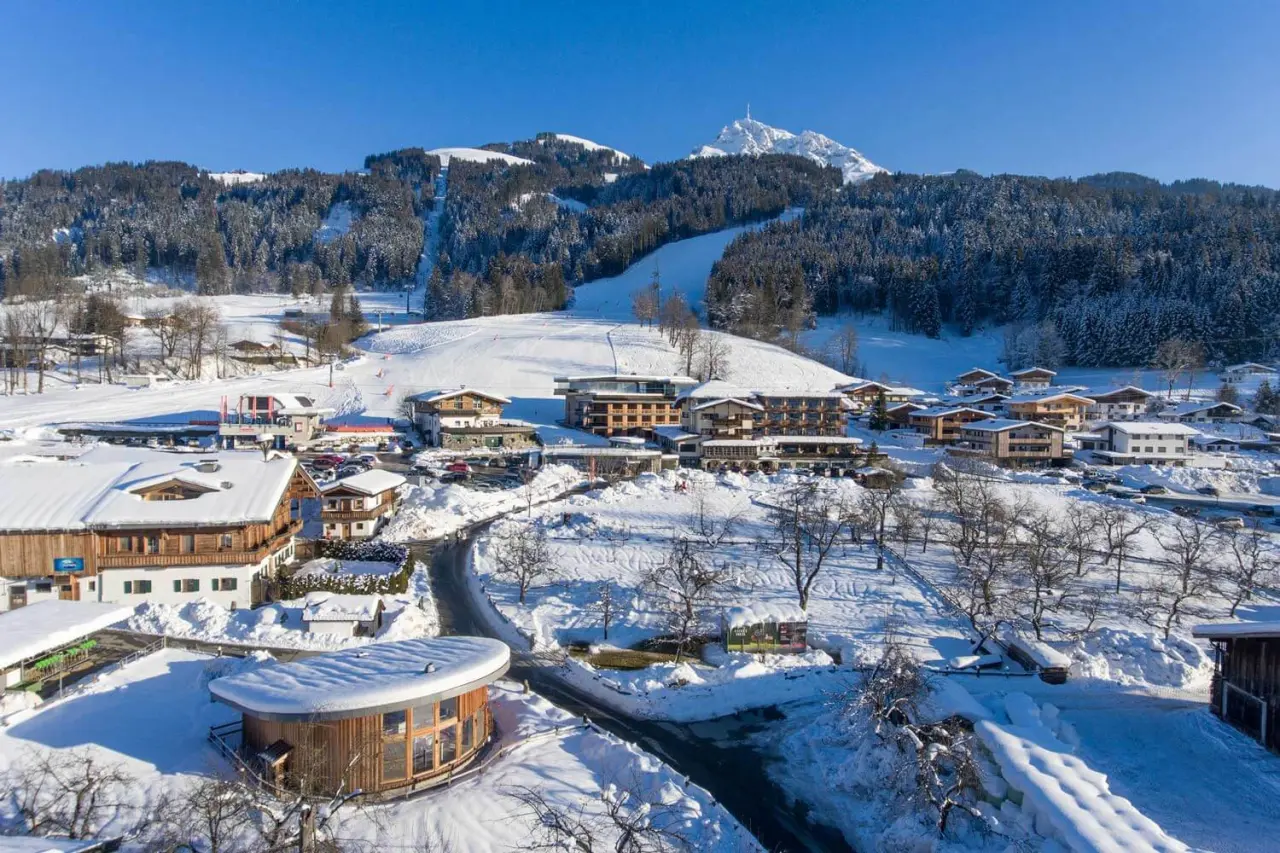 Hotel Penzinghof im Winter, umgeben von verschneiten Bergen und Skipisten unter blauem Himmel.