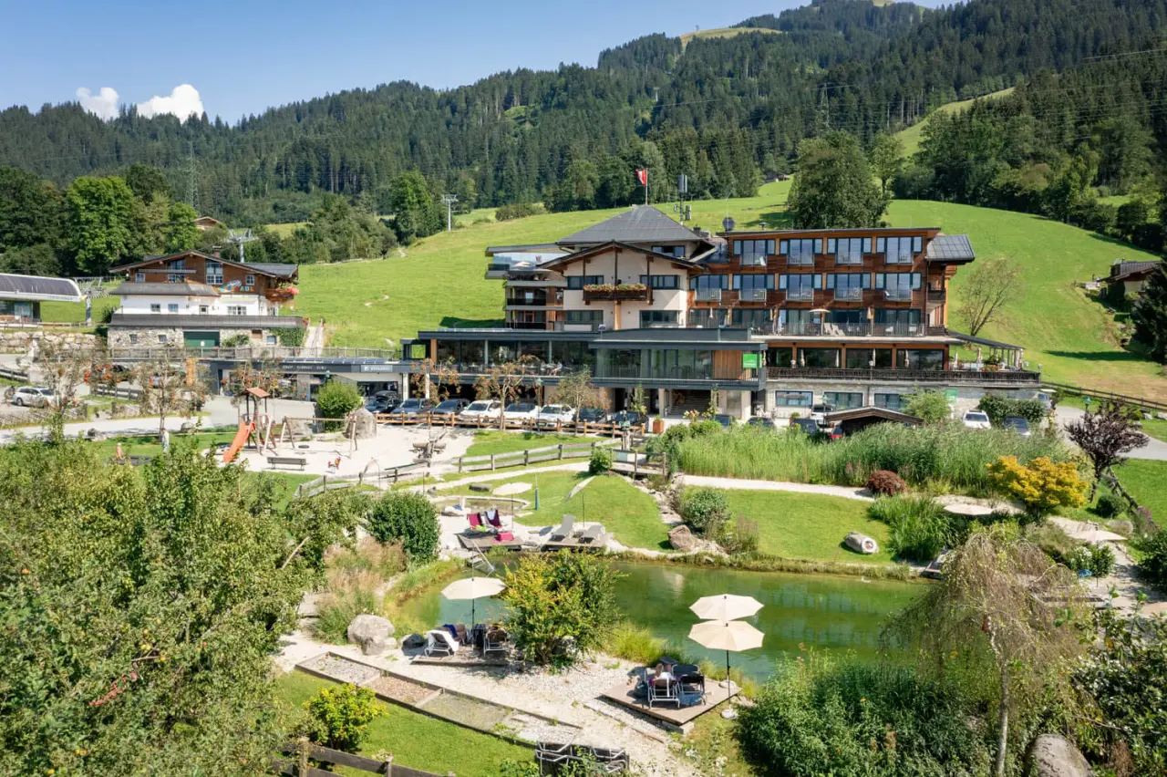 Panoramablick auf das Hotel Penzinghof mit Naturteich und Berglandschaft in den Kitzbüheler Alpen.