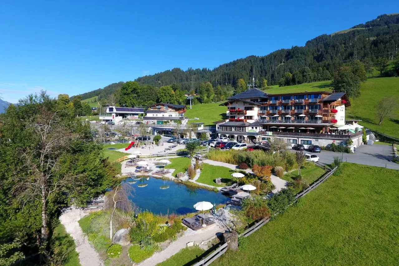 Hotel Penzinghof: Idyllische Luftaufnahme mit Natur-Badeteich, Liegewiesen und Alpenpanorama in den Kitzbüheler Alpen.