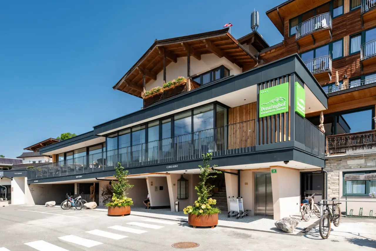 Aussenansicht des modernen Hotel Penzinghof mit alpiner Architektur, Holzelementen und Balkonen unter blauem Himmel.
