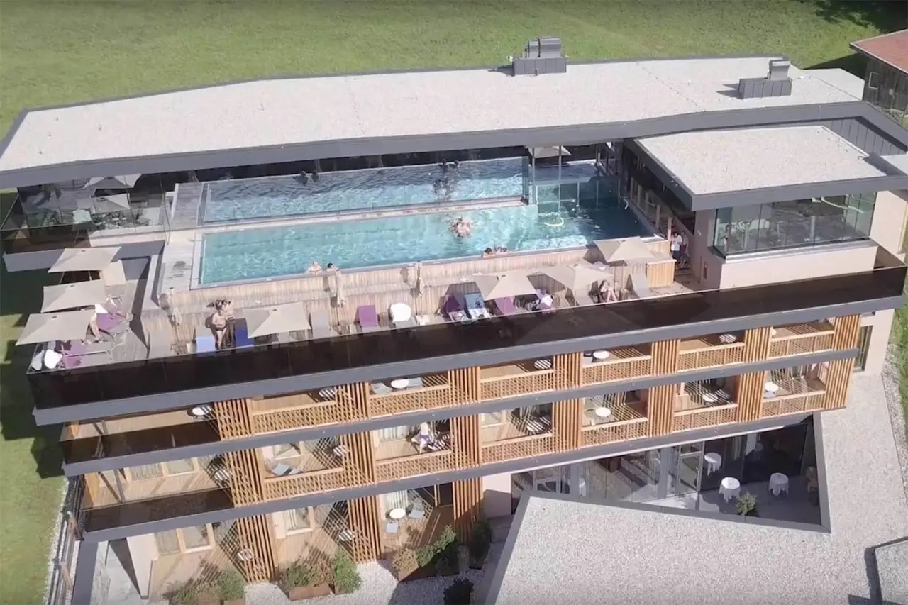 Dachpool und Sonnenterrasse mit Gästen auf dem modernen Hotel Penzinghof. Panoramablick auf die Wellness-Anlage.