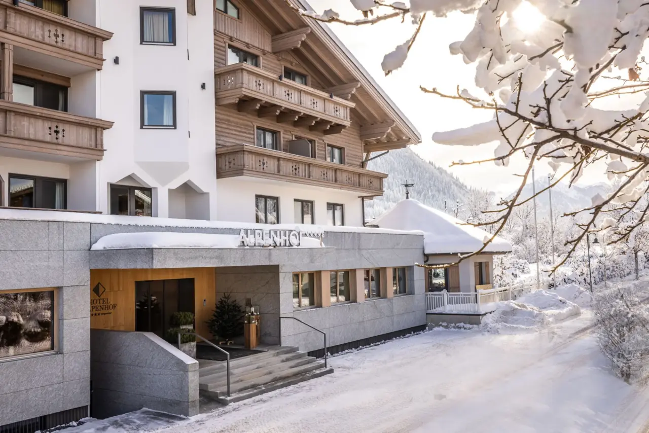 Design & Wellness Hotel Alpenhof im Winter mit schneebedeckten Balkonen und Ästen, umgeben von einer idyllischen Berglandschaft.
