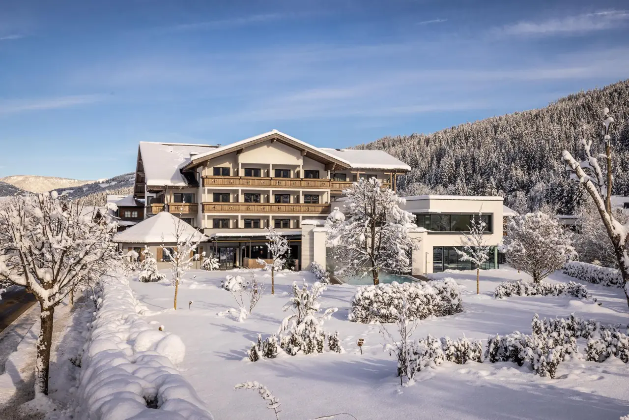 Design & Wellness Hotel Alpenhof im Winter. Traditionelle Architektur umgeben von tief verschneiter Landschaft und Wald.