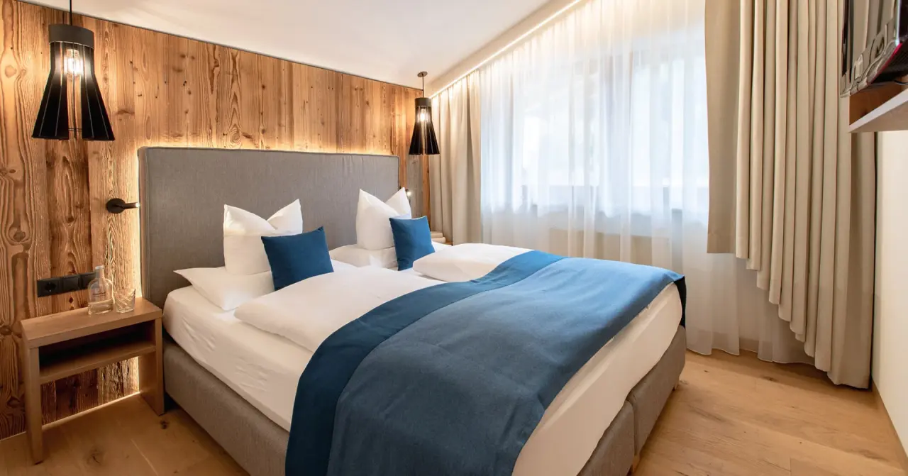 Modernes Doppelzimmer mit Holzwand, indirekter Beleuchtung und blauen Akzenten im Design & Wellness Hotel Alpenhof.