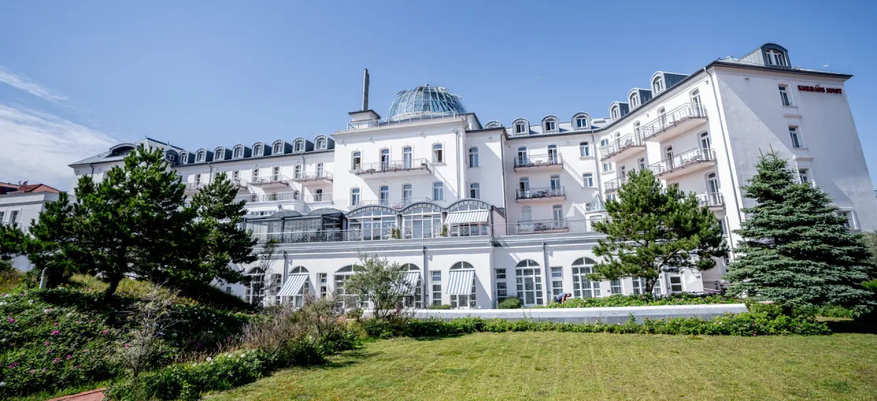 Majestätische Aussenansicht des historischen Strandhotel Kurhaus Juist unter blauem Himmel mit grünen Dünen.