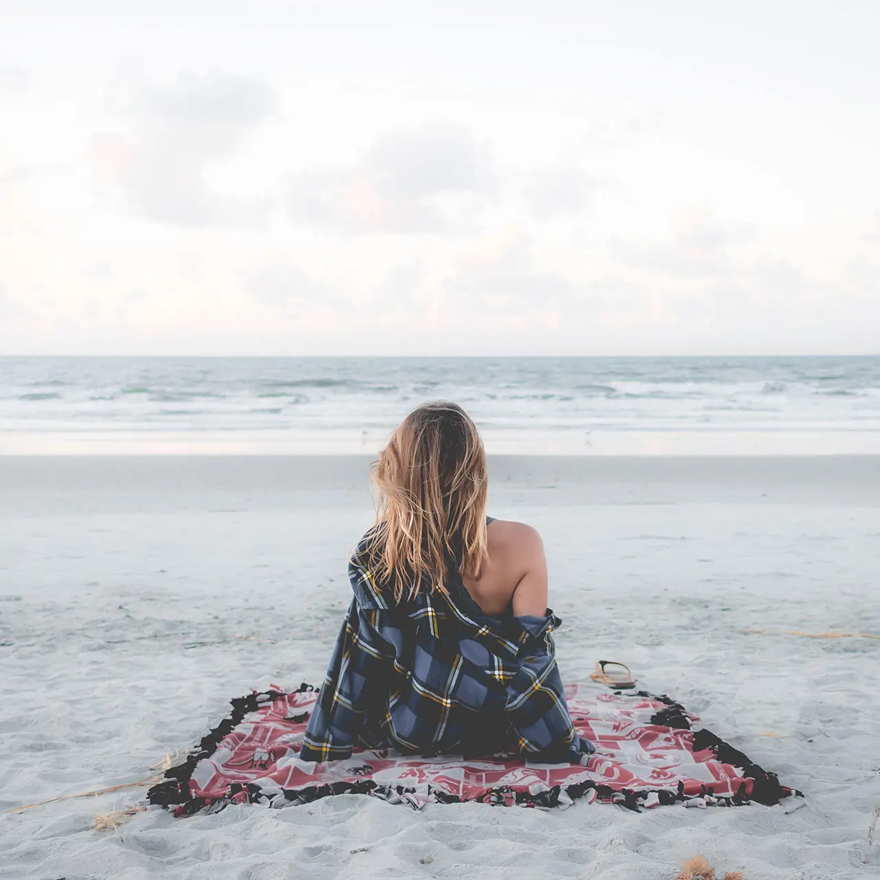 Rückenansicht einer Frau, die am Sandstrand von Juist entspannt und auf die Nordsee blickt, nahe dem Strandhotel Kurhaus Juist.