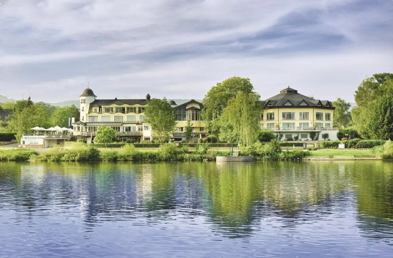 Aussenansicht des Hotel Weisser Bär am Flussufer mit grüner Landschaft und Spiegelung im Wasser.