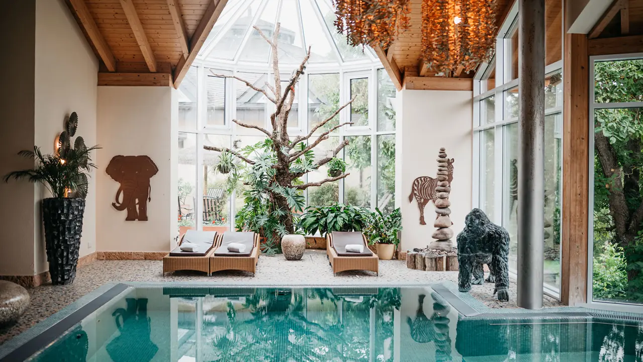 Exotischer Poolbereich mit Liegen, Pflanzen und Safari-Dekoration unter Glasdach im Hotel Weisser Bär.