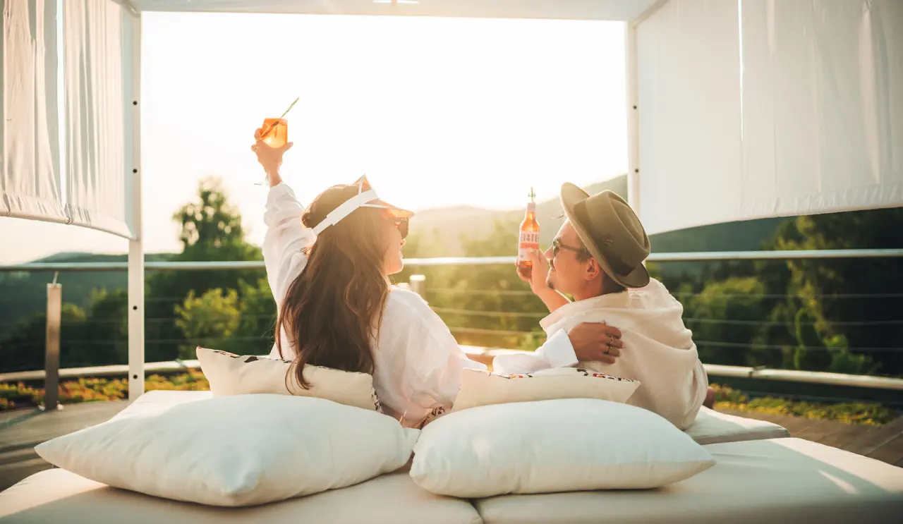 Paar genießt Cocktails auf einer Sonnenterrasse mit Bergblick im Thula Wellnesshotel Bayerischer Wald.