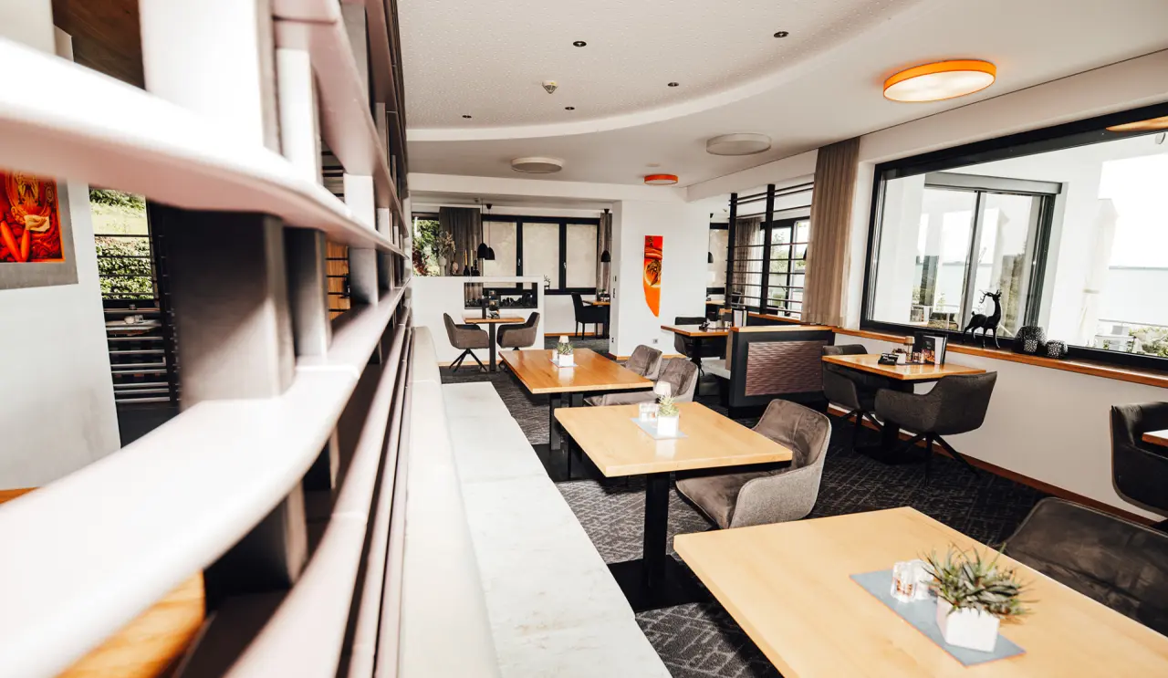 Modernes Restaurant im Thula Wellnesshotel Bayerischer Wald mit Holztischen, bequemen Stühlen und großen Fenstern.