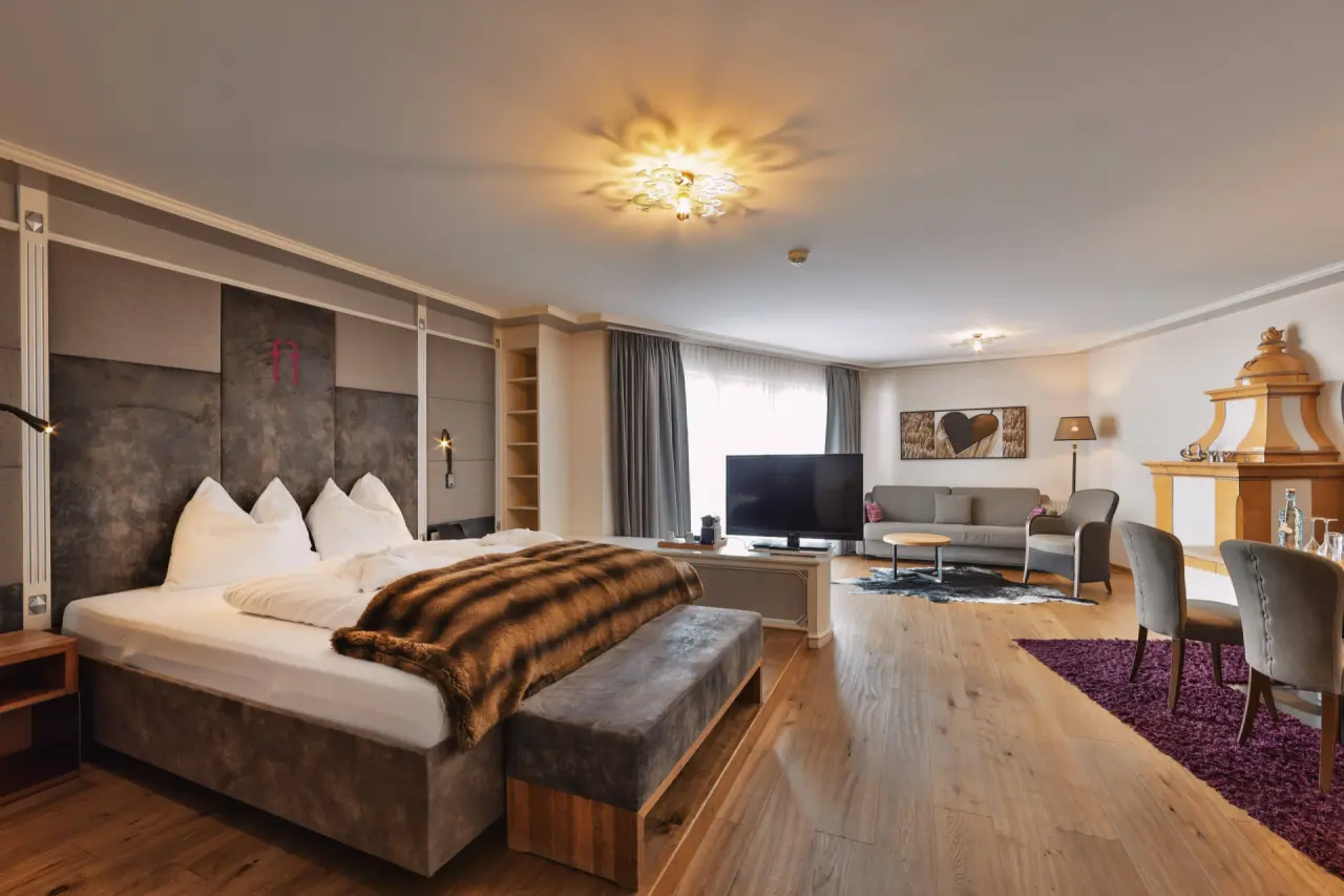 Geräumiges Hotelzimmer im Hotel Fliana mit großem Bett, gemütlicher Sitzecke, TV und traditionellem Kachelofen.