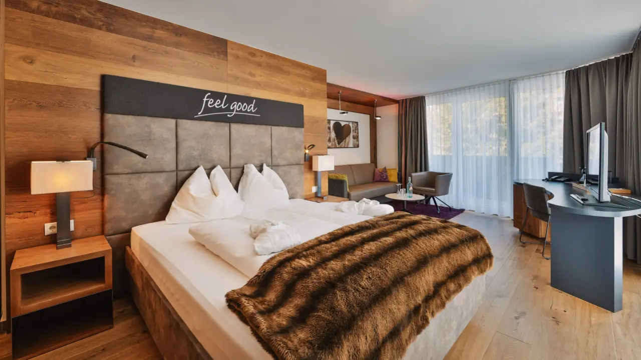 Modernes Doppelzimmer im Hotel Fliana mit Holzwand, großem Bett, Sitzgelegenheit und Schreibtisch für Komfort und Entspannung.