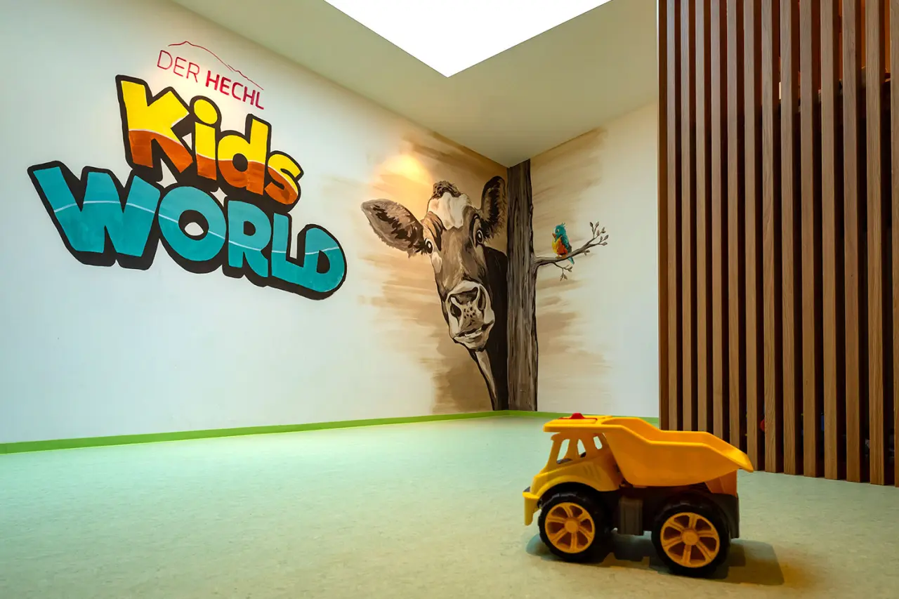 Spielbereich 'Kids World' im Hotel DER HECHL mit bunter Wandmalerei einer Kuh und Spielzeug für Kinder.