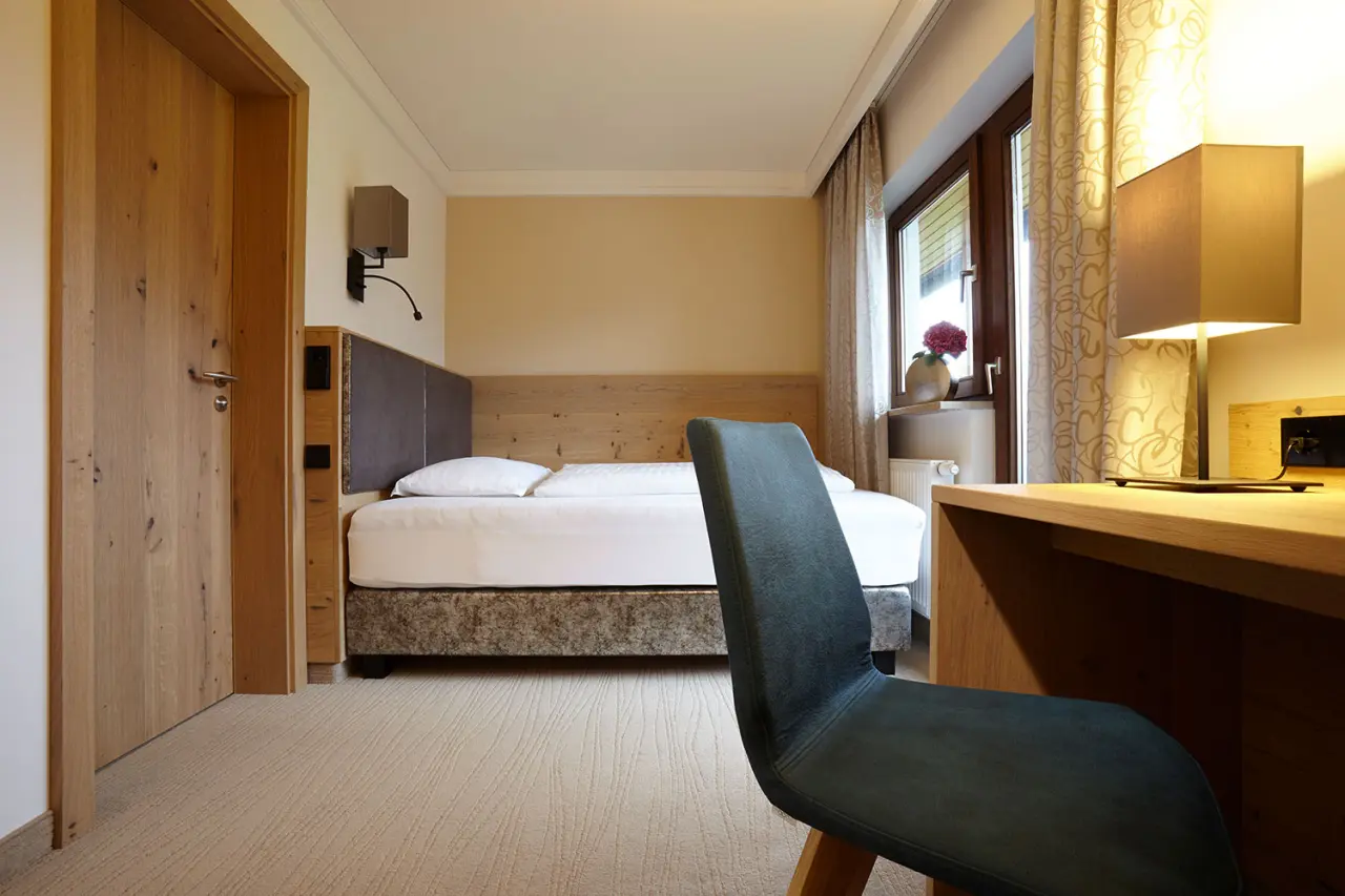 Gemütliches Doppelzimmer im Hotel DER HECHL mit Holzelementen, bequemen Bett und Schreibtischbereich am Fenster.