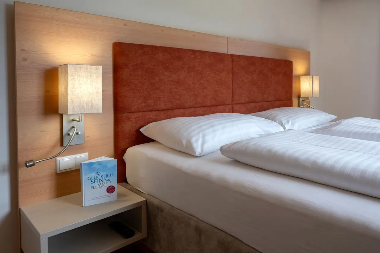 Gemütliches Doppelbett mit Holzvertäfelung und Leselampen im Hotel DER HECHL.
