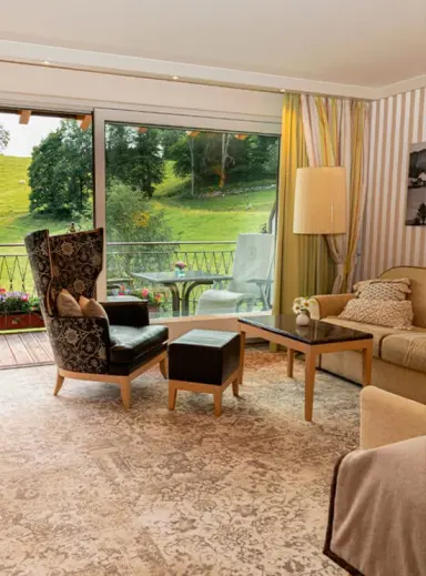 Geräumiges Hotelzimmer im Hotel Kesslermühle mit gemütlicher Sitzecke, Balkon und idyllischem Blick auf die grüne Landschaft.