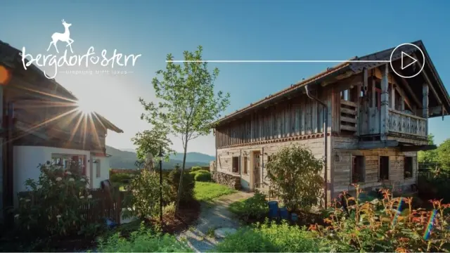 Sonnenbeschienene traditionelle Holzhäuser des Bergdorf Sterr mit Bergpanorama und Garten im Abendlicht.