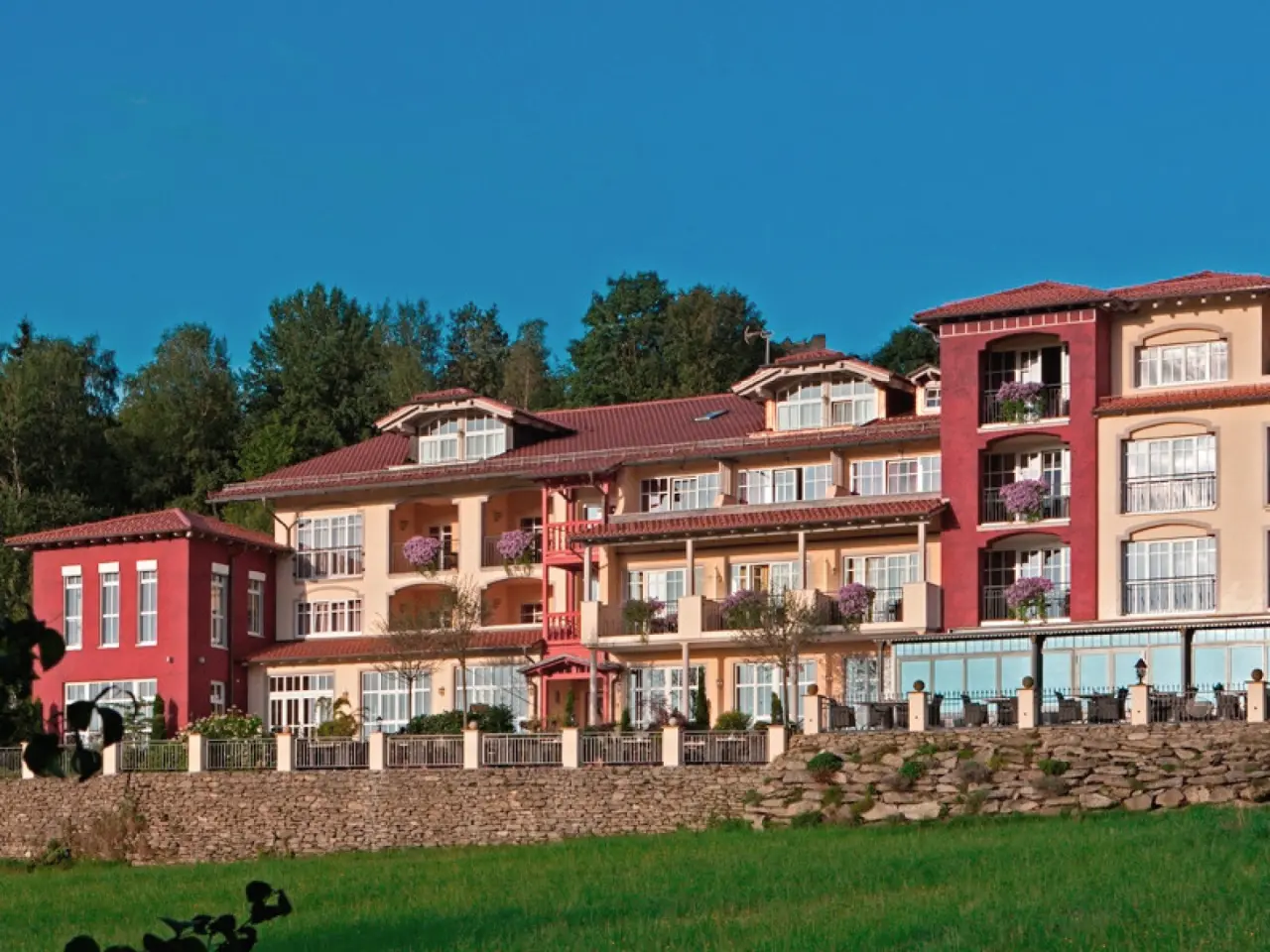 Aussenansicht des Burghotel Sterr mit farbenfroher Fassade, roten Dächern und grüner Umgebung unter blauem Himmel.
