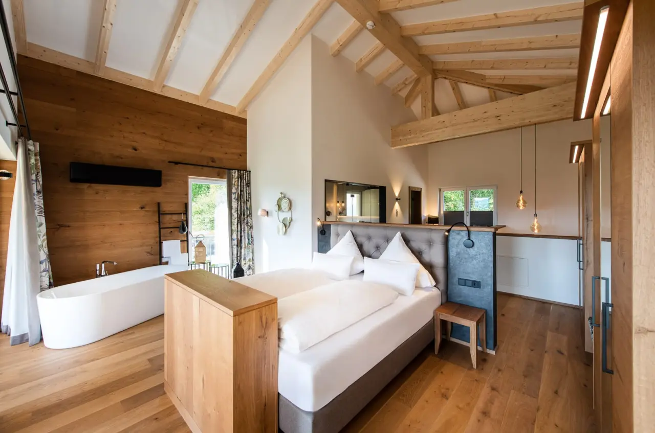 Geräumiges Hotelzimmer im Burghotel Sterr mit freistehender Badewanne, Holzbalken und gemütlichem Doppelbett.