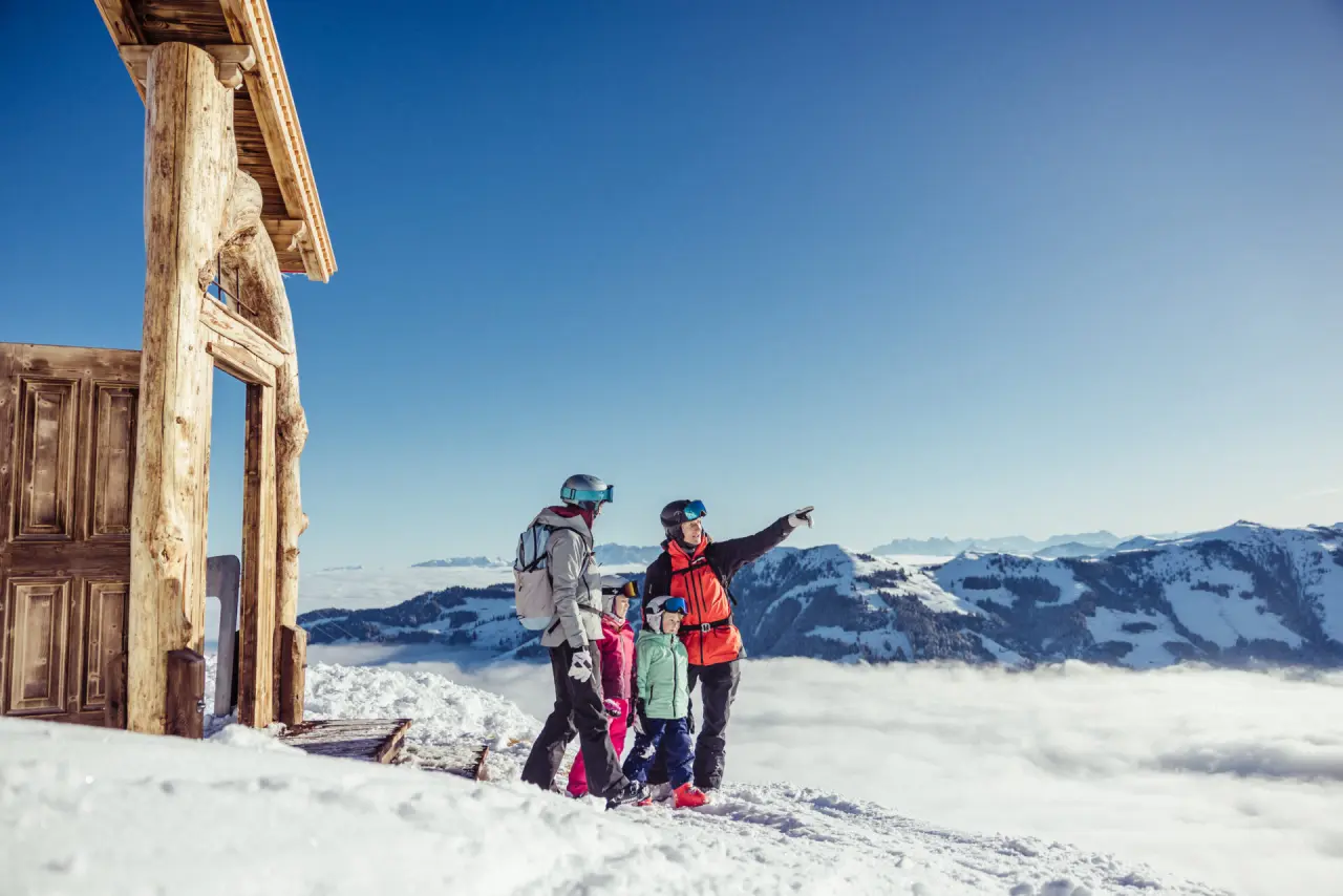 Familie in Skiausrüstung genießt den Panoramablick auf verschneite Alpen und Wolkenmeer am Galtenberg Resort 4*S.