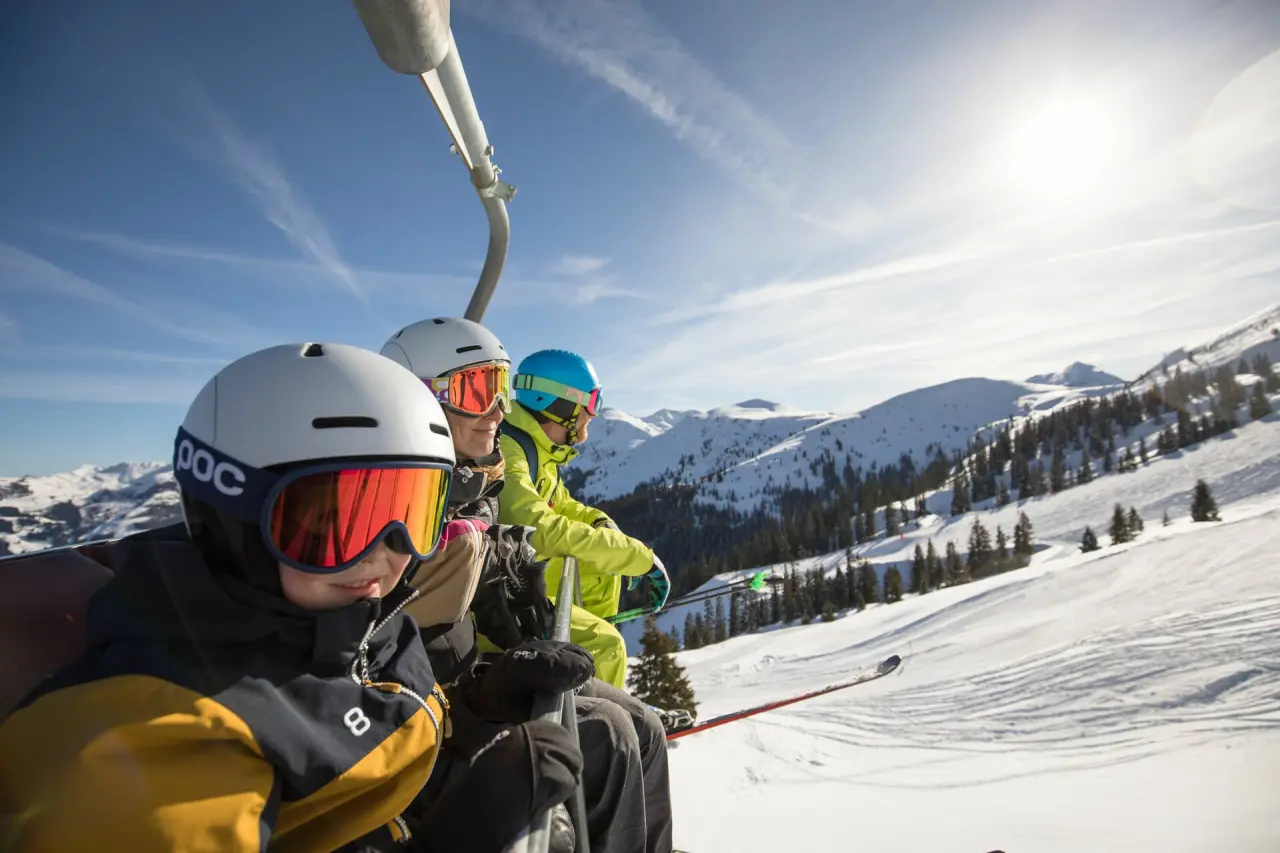 Familie auf dem Skilift mit Blick auf die verschneiten Alpen im Galtenberg Resort 4*S. Winterurlaub in den Bergen.