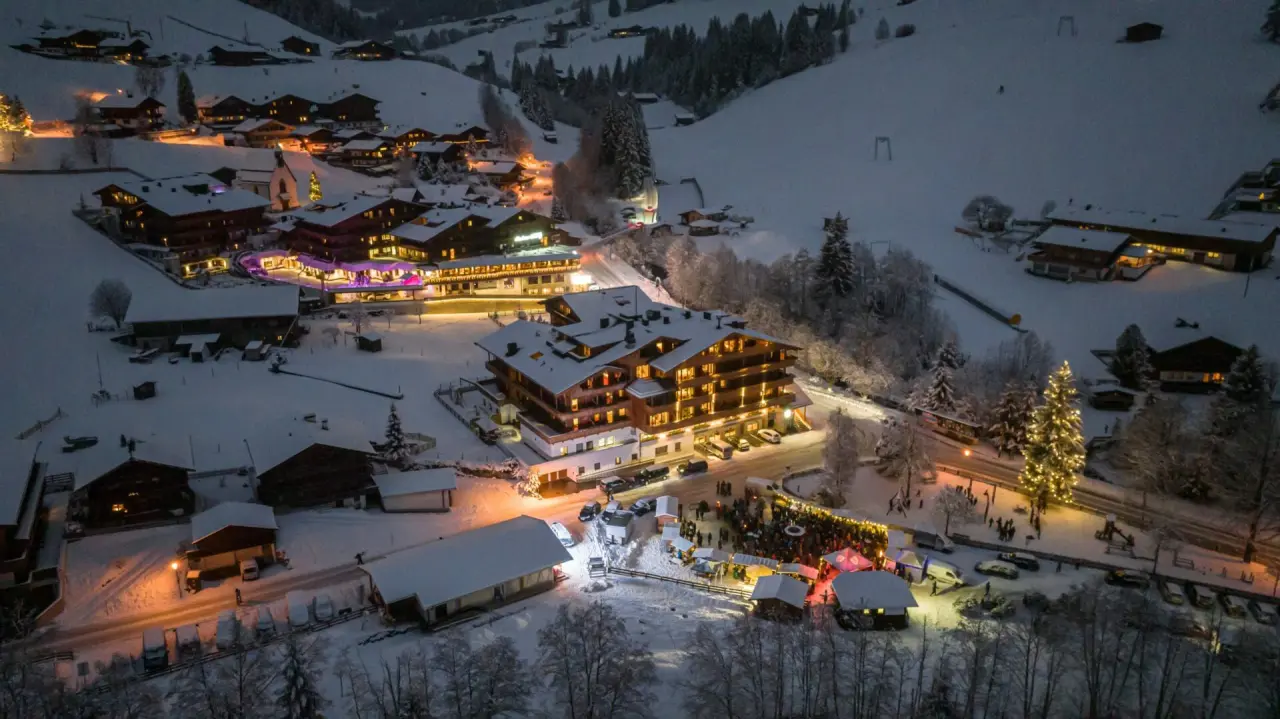 Winterliche Luftaufnahme des Galtenberg Resort 4*S in den verschneiten Alpen bei Nacht, mit festlicher Beleuchtung und Dorfleben.