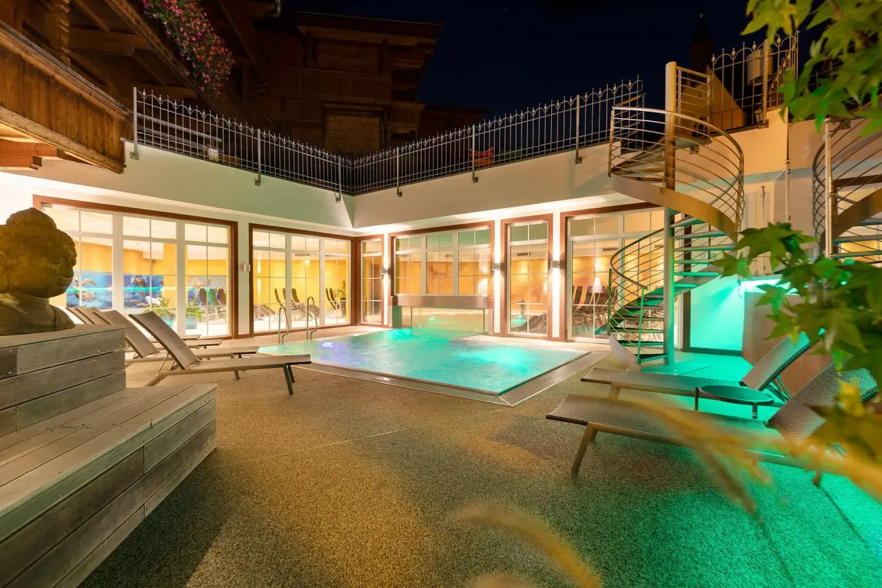 Beleuchteter Aussenpool mit Liegen und Buddha-Statue im Wellnessbereich des Galtenberg Resort 4*S bei Nacht.